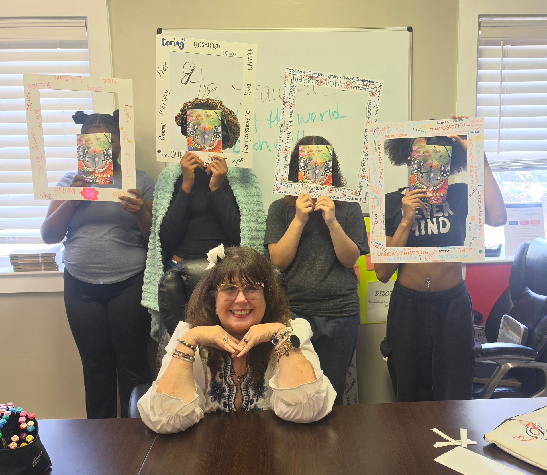 Michelle seated at a table with four students standing behind her, each holding a decorated frame covered in positive affirmations