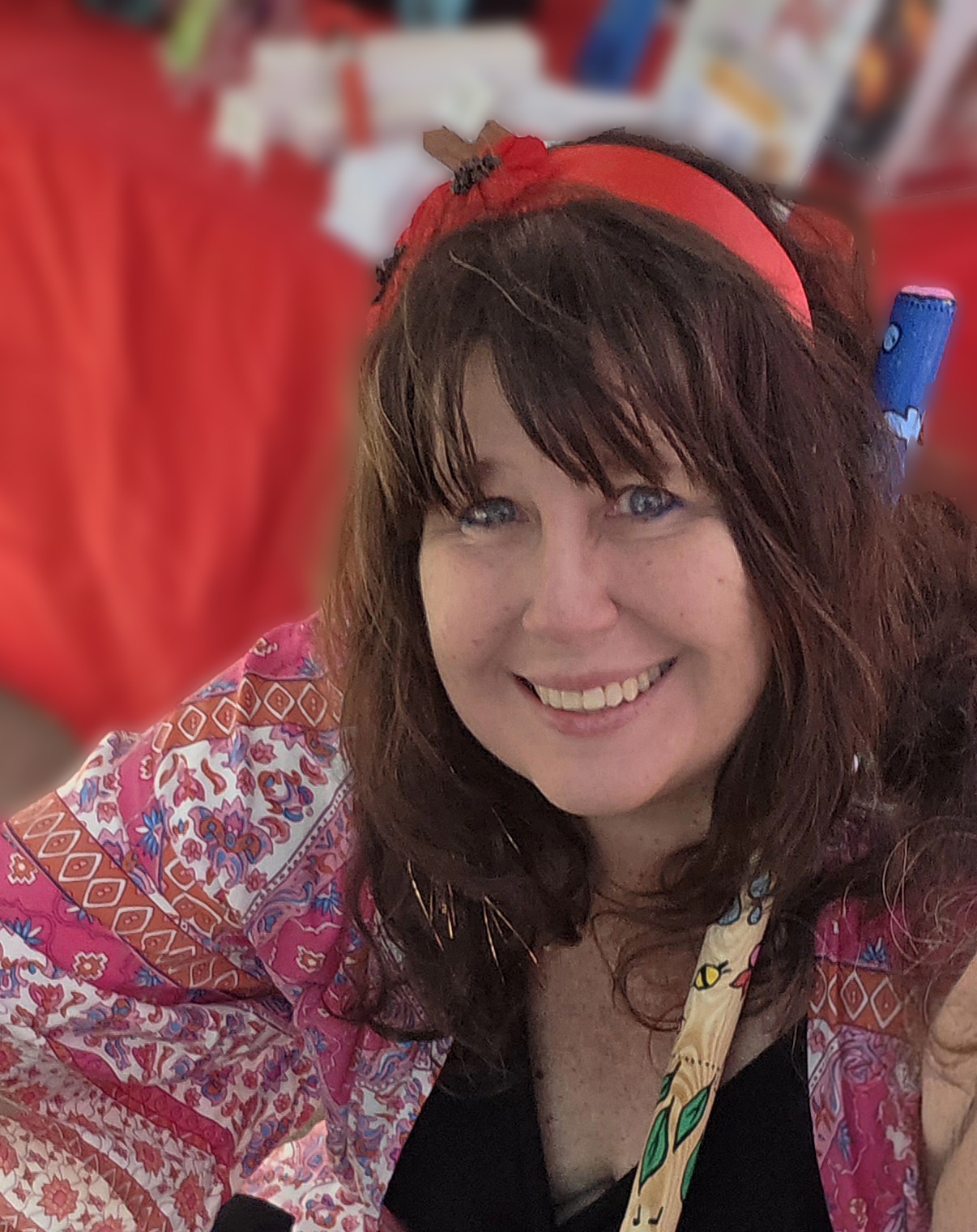 Michelle smiling warmly at the camera in a patterned blouse and red headband, with a blurred red backdrop