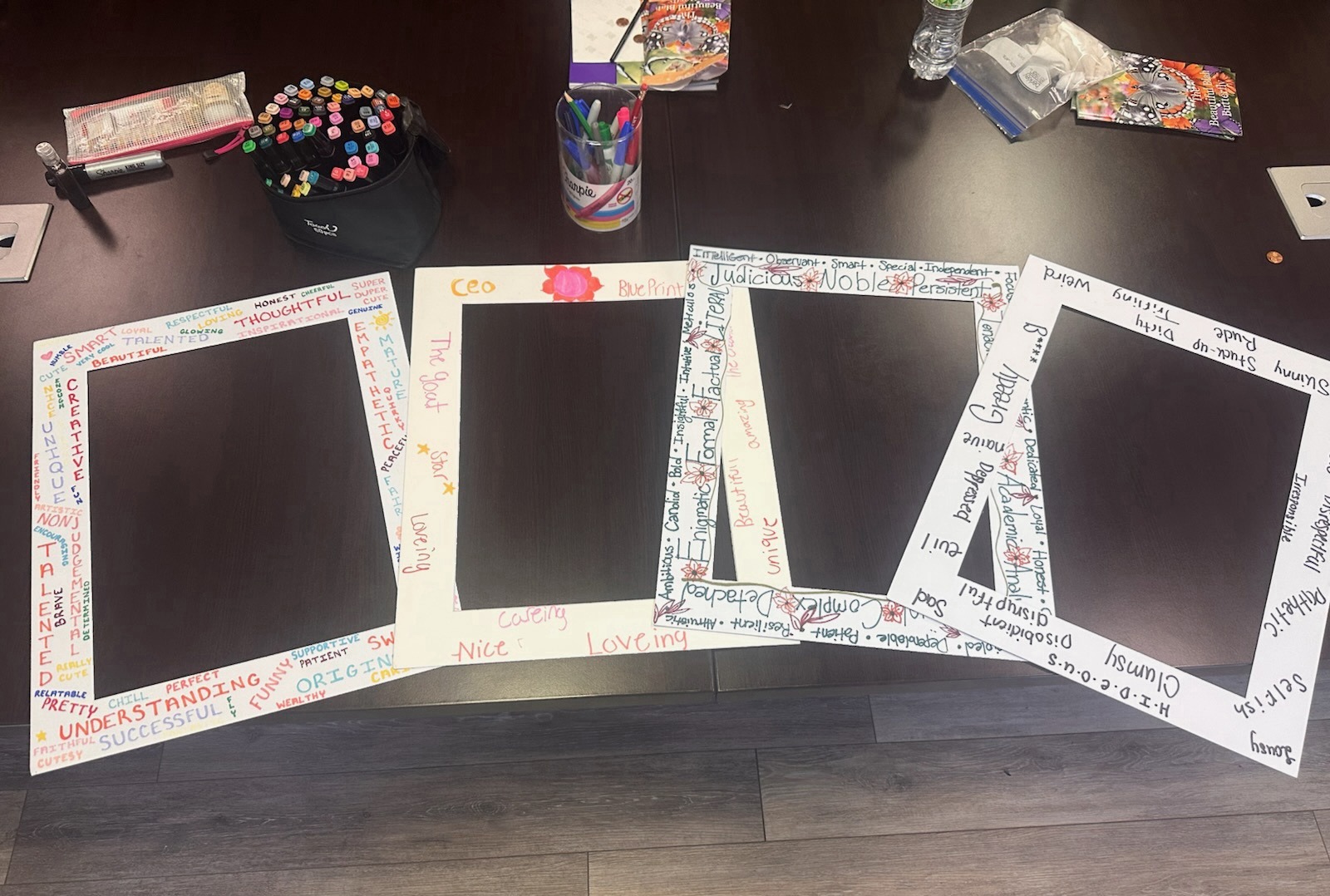 Four decorated picture-frame mats covered in handwritten positive and negative words, laid out on a table